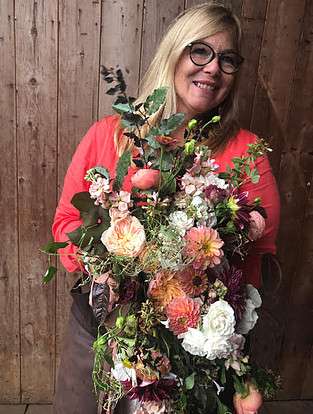 Floral designer holding a cascading arrangement of garden roses and dahlias