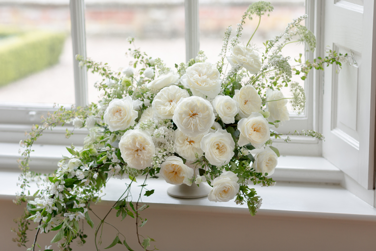 An arrangement of white garden roses and fine white blossom on a windowsill.