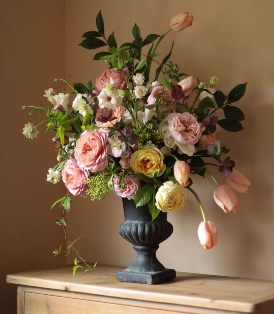 Garden rose and tulip arrangement in black urn on wood table
