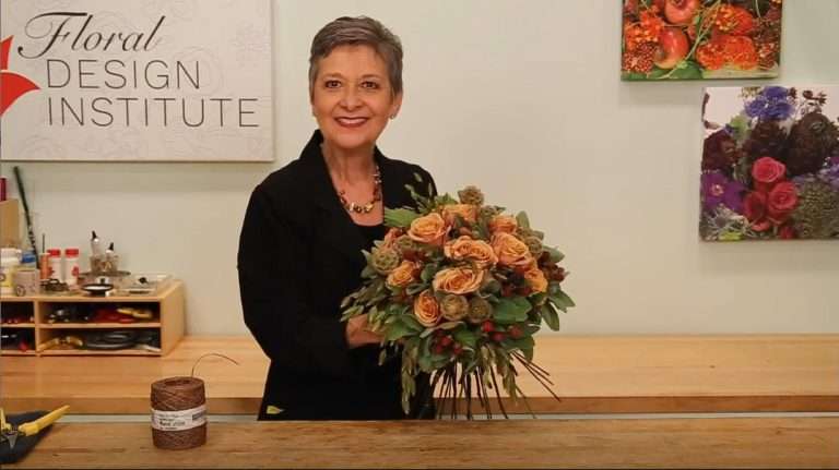 A floral designer holding an autumn arrangement of orange garden roses in a studio.