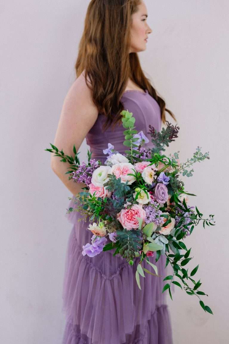 A person in a lilac gown holding a loose bouquet of pink and cream garden roses.