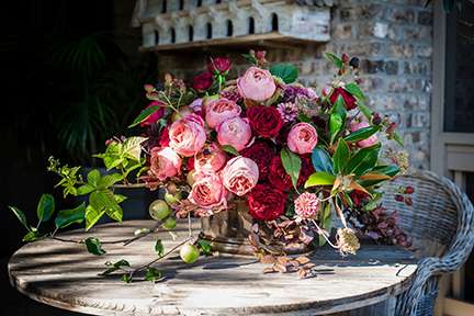 Deep pink and red garden rose centerpiece on rustic outdoor table