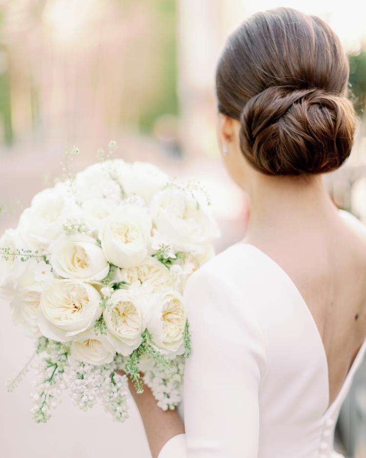 Bride's low bun and back of gown beside a lush ivory garden rose bouquet