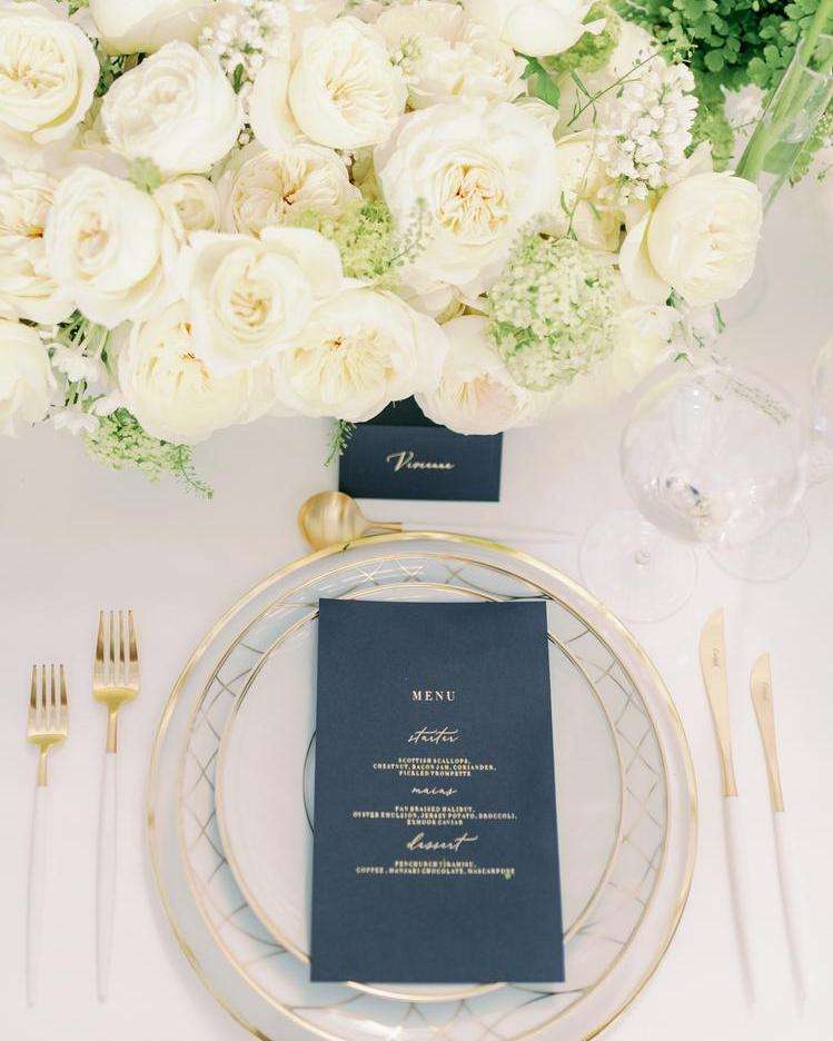 Overhead view of ivory garden rose centerpiece beside navy menu place setting