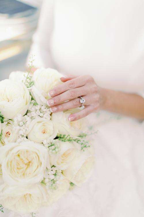 Bride's hand with engagement ring resting on ivory garden rose bouquet