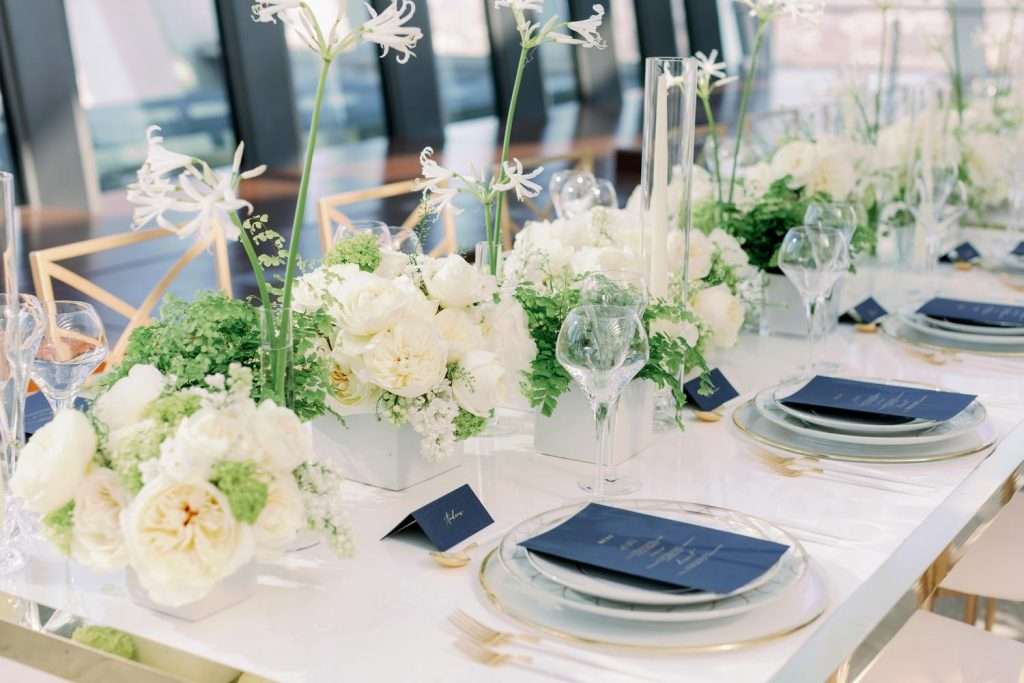 Long reception table lined with white garden rose arrangements and navy menus