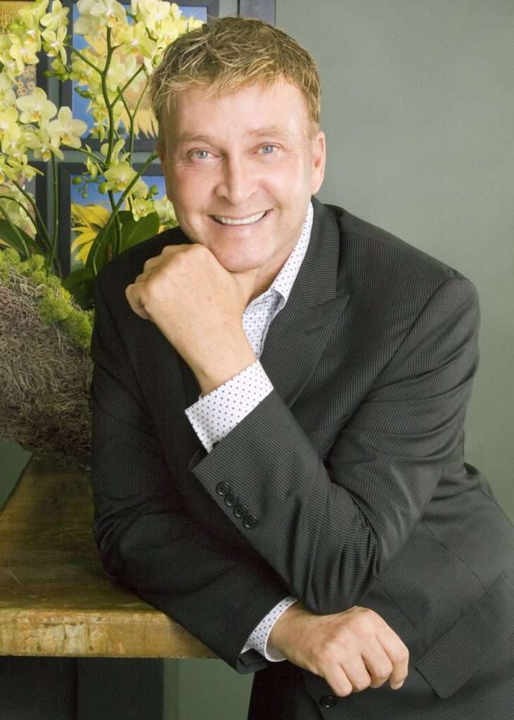 Rene van Rems poses beside an orchid arrangement