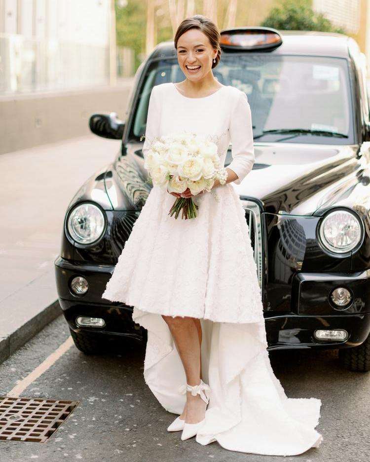 Bride in white dress holding ivory garden rose bouquet by a London black cab
