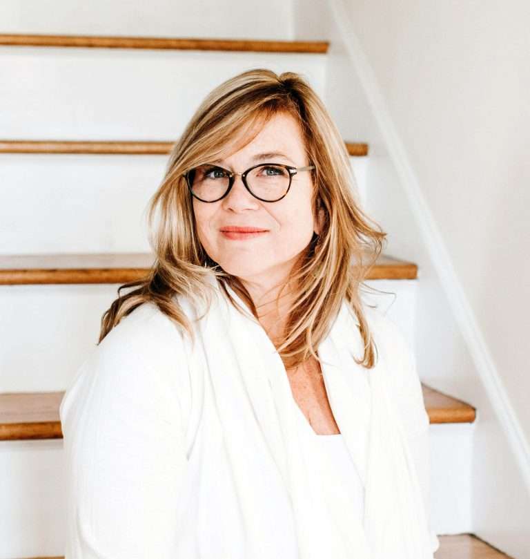 A person in a white shirt standing at the foot of a staircase.