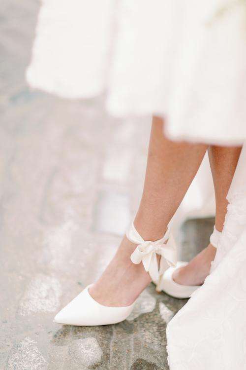 Bride's white bow-tie heels beneath her lace wedding gown