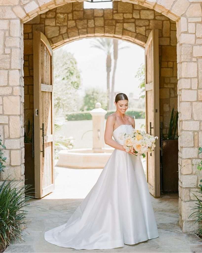 Bride in a strapless gown holding her bouquet under a stone archway