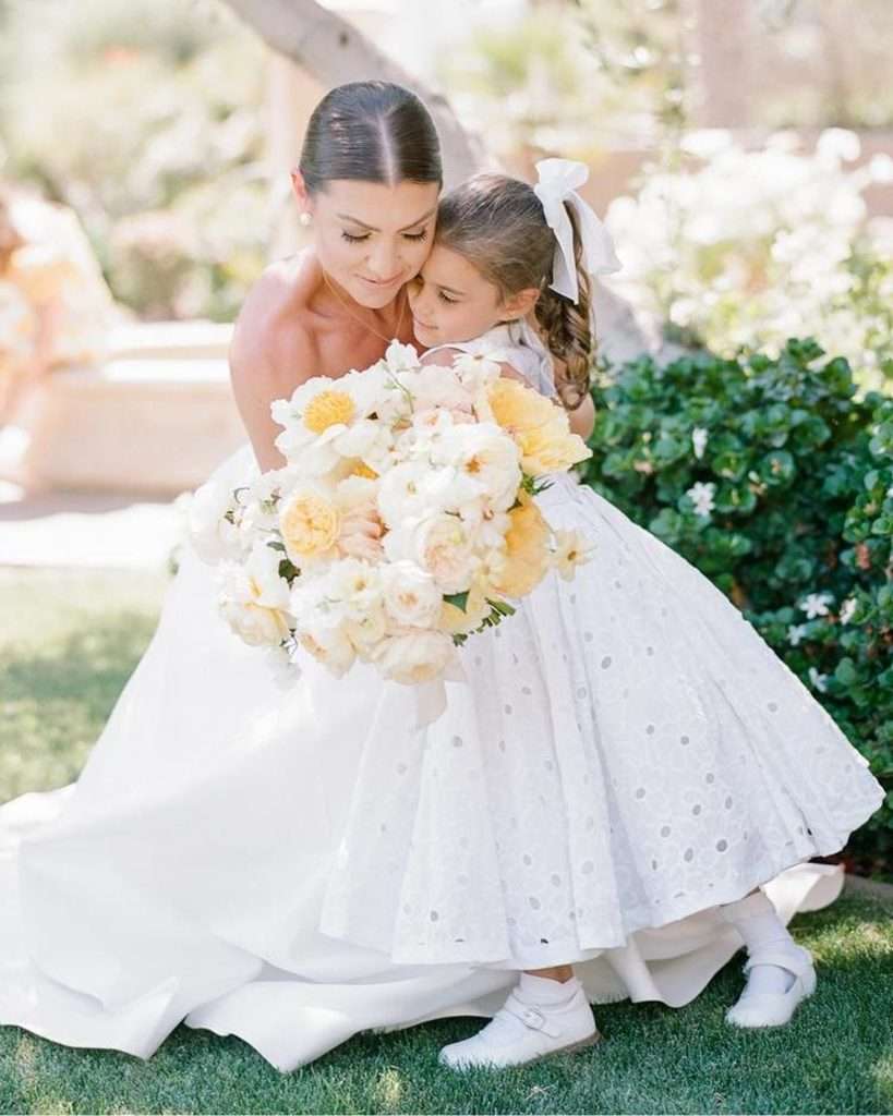 Bride embracing the flower girl in a white eyelet dress