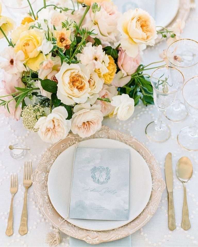 A place setting with gold cutlery beside an arrangement of cream and yellow garden roses, seen from above.
