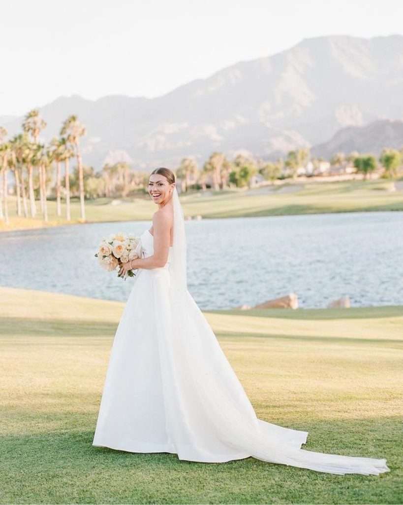 Bride looking back over her shoulder on the lawn beside the lake