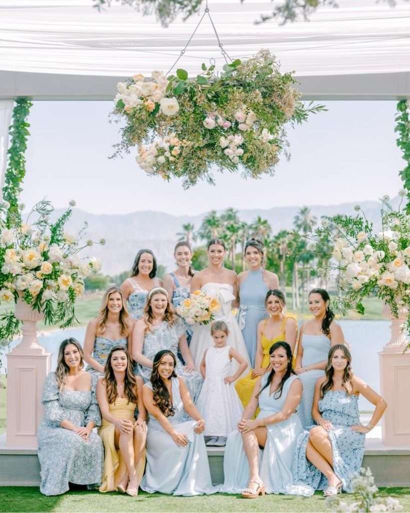 Bride and bridesmaids in dusty blue and yellow dresses posed under the pavilion
