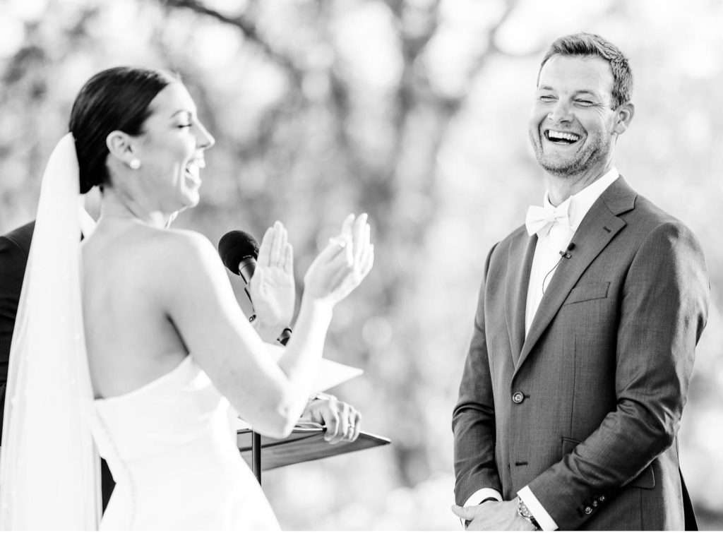 Black and white photo of the bride laughing with the groom at the altar