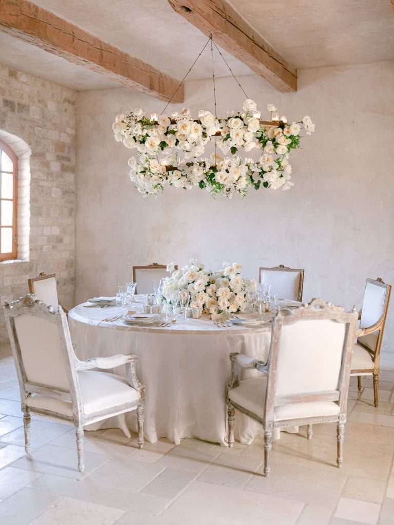 A hanging floral wreath above a round table set for a winter wedding in a stone room.