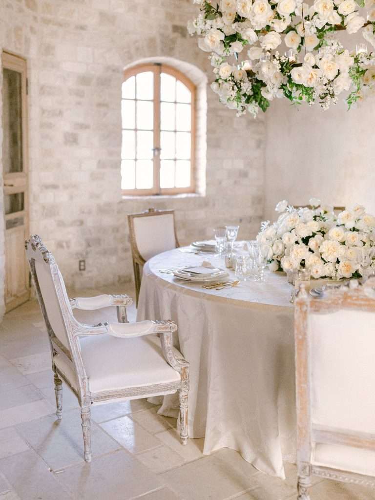 Rustic stone dining room set for a wedding with an overhead white garden rose chandelier