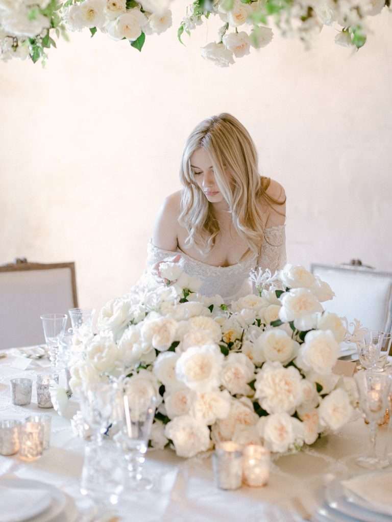Bride arranging a lush white garden rose table runner beside candlelight