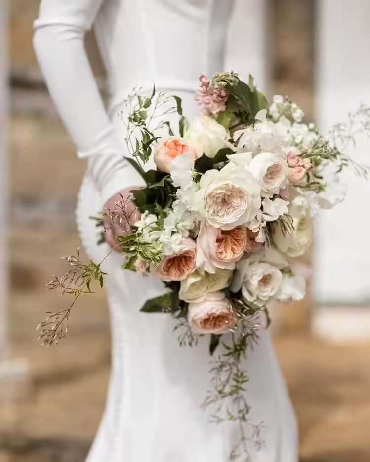 Bride in a fitted gown holding a cascading white and peach garden rose bouquet