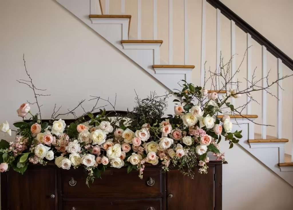 Ivory and blush garden roses with bare branches atop an antique wood cabinet