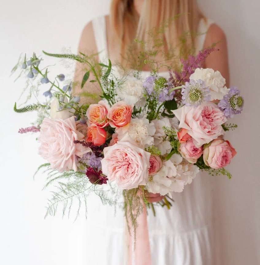 Bride holding pastel pink and lavender garden rose bouquet with trailing ribbon