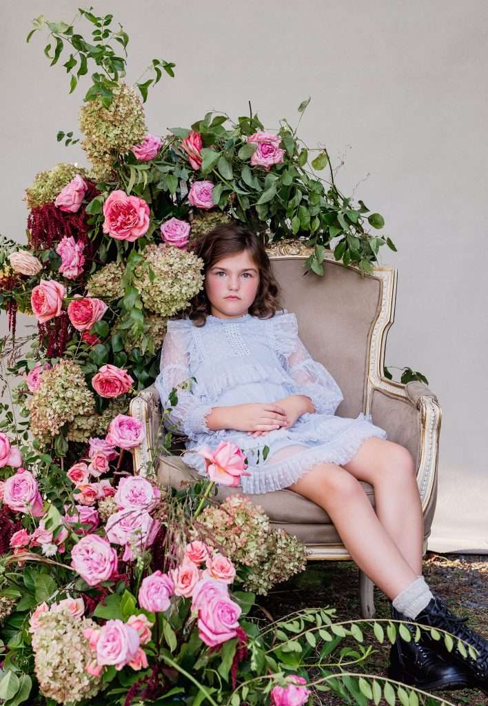 Child seated beside a pink garden rose and hydrangea floral installation