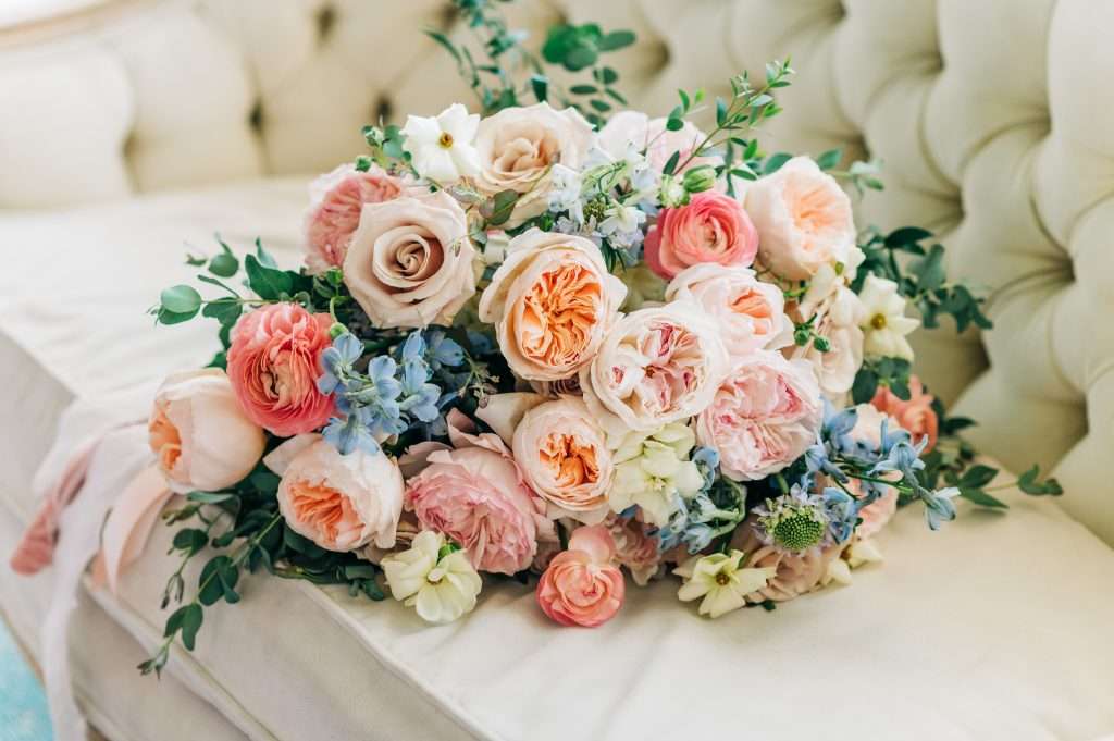 Peach and blush garden rose bouquet with delphinium on a tufted settee