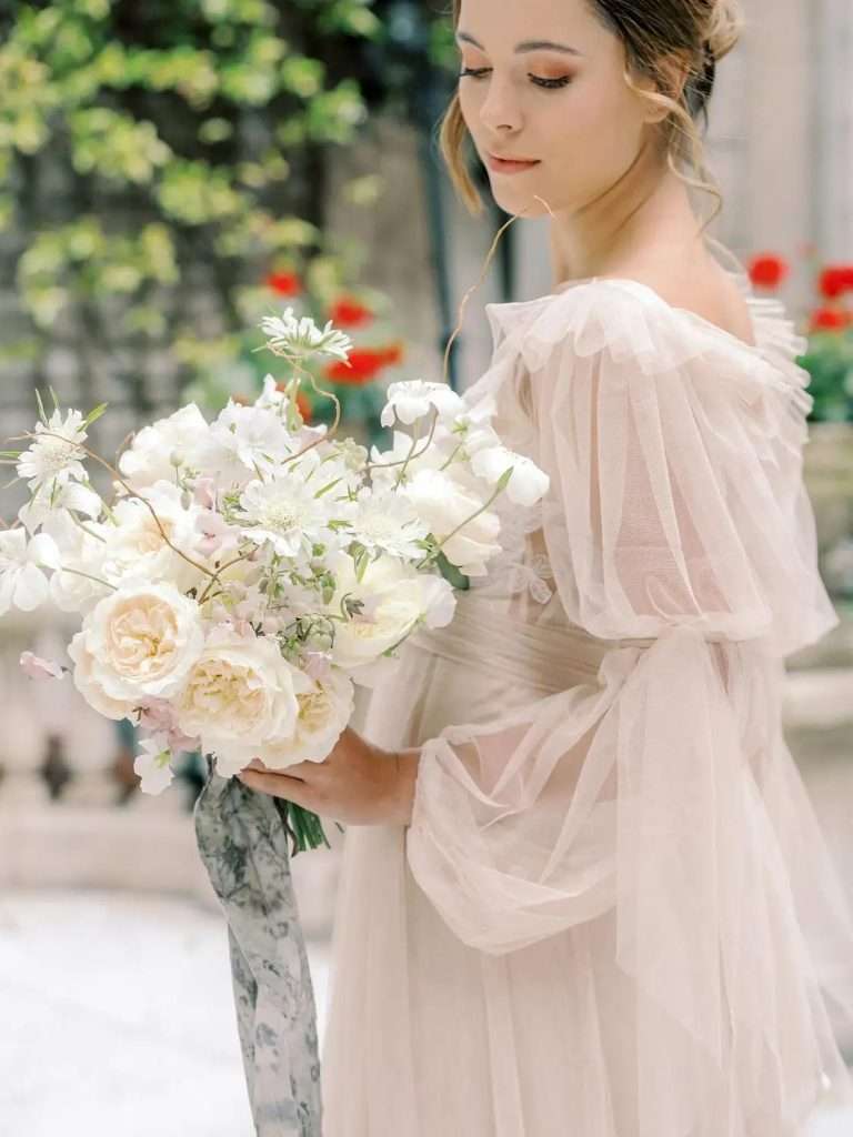 A person in a blush gown holding a bouquet of cream and white garden roses.
