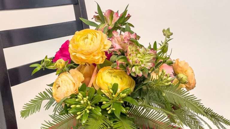 Yellow and pink garden rose arrangement with fern resting on a dark chair