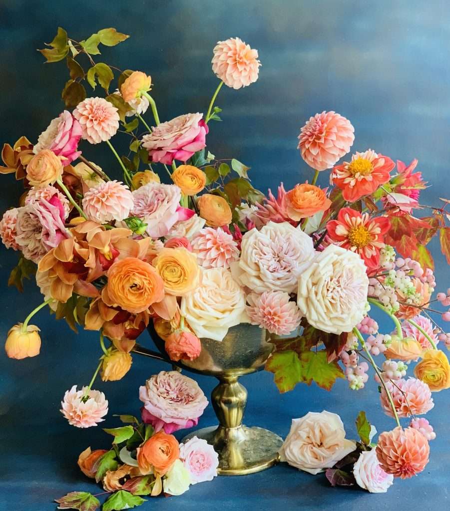 Autumnal arrangement of garden roses and dahlias in a gold compote against blue
