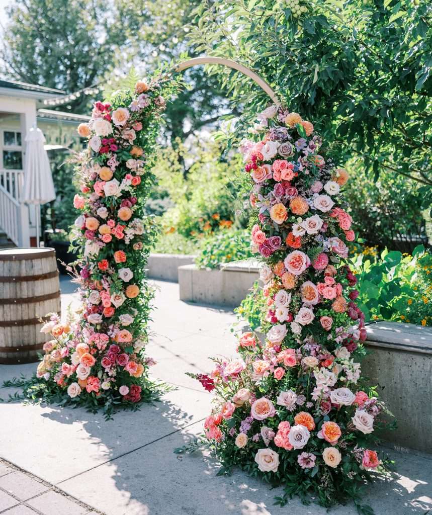 Twin garden rose columns in pink, peach and coral flanking an outdoor entrance
