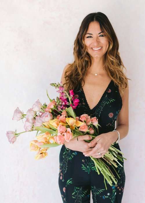 Florist smiling while holding a lush bouquet of pink and peach garden roses