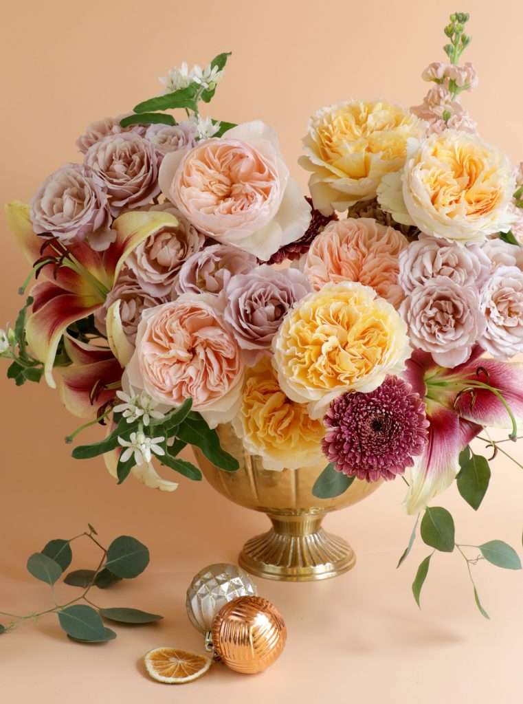 Mauve and peach garden rose arrangement with lilies in a gold urn