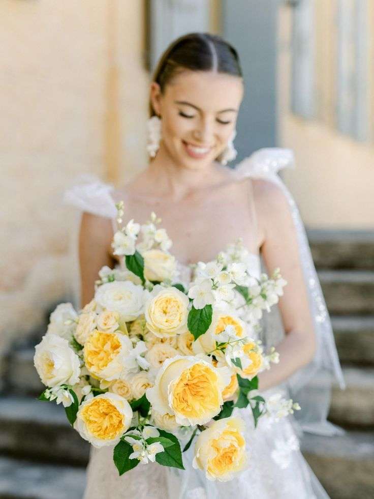 Bride in a lace gown cradling a yellow and cream garden rose bouquet