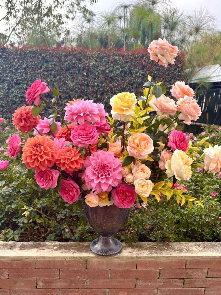 Urn arrangement of pink and peach garden roses with dahlias in a garden setting