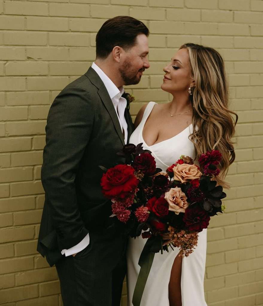 Bride and groom embrace with a moody burgundy garden rose and dahlia bouquet