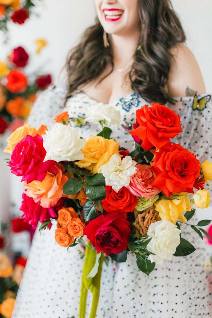 Bride laughing while holding a vibrant red, orange and white garden rose bouquet