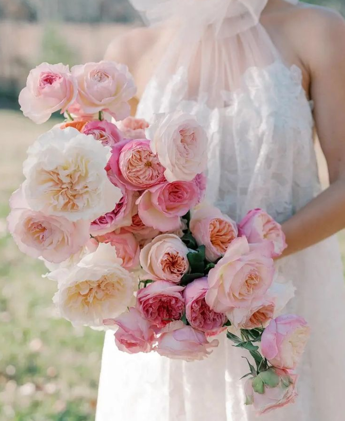 A bouquet of blush and peach garden roses held against a sheer wedding gown.