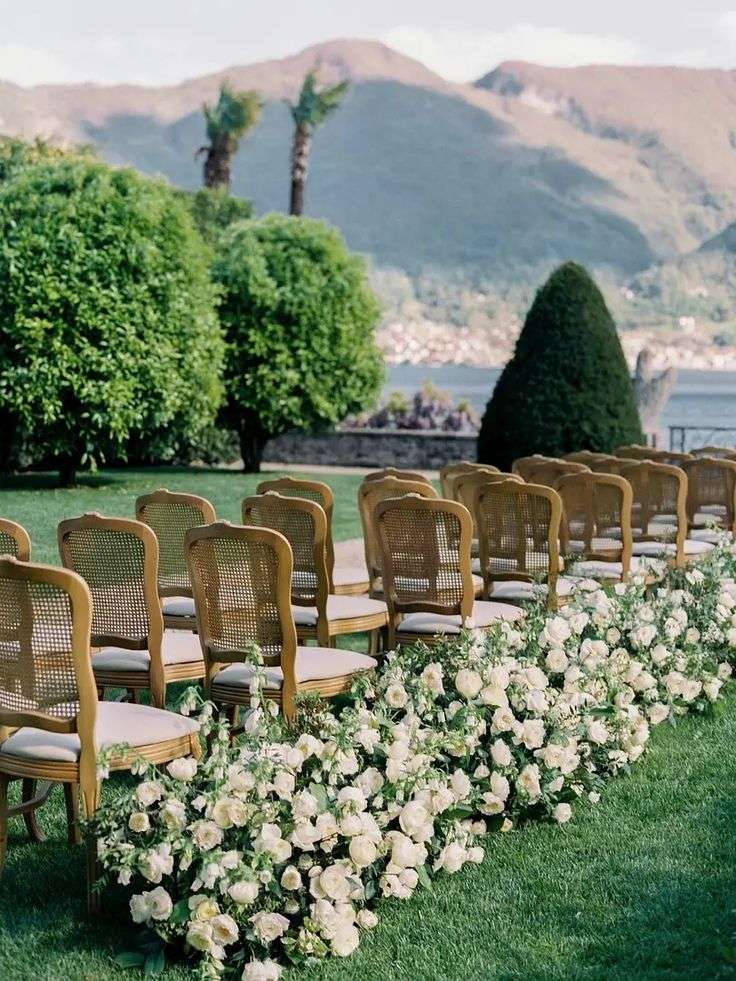 Ceremony aisle lined with white garden roses and cane chairs overlooking a lake