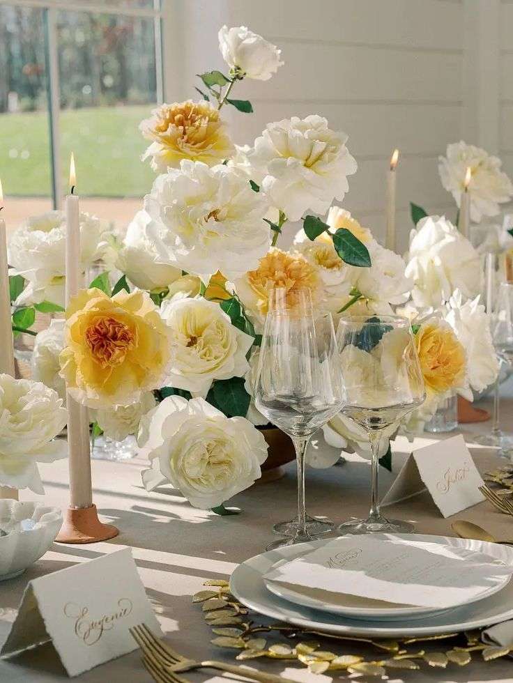 Reception table set with candles beside a cluster of white and yellow garden roses