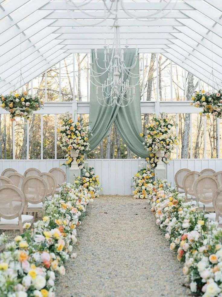 Greenhouse ceremony aisle with yellow and blush garden rose borders and hanging chandelier