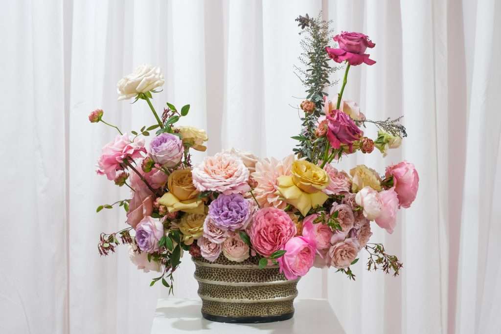 Finished arrangement of pink, purple and yellow garden roses in a hammered vase