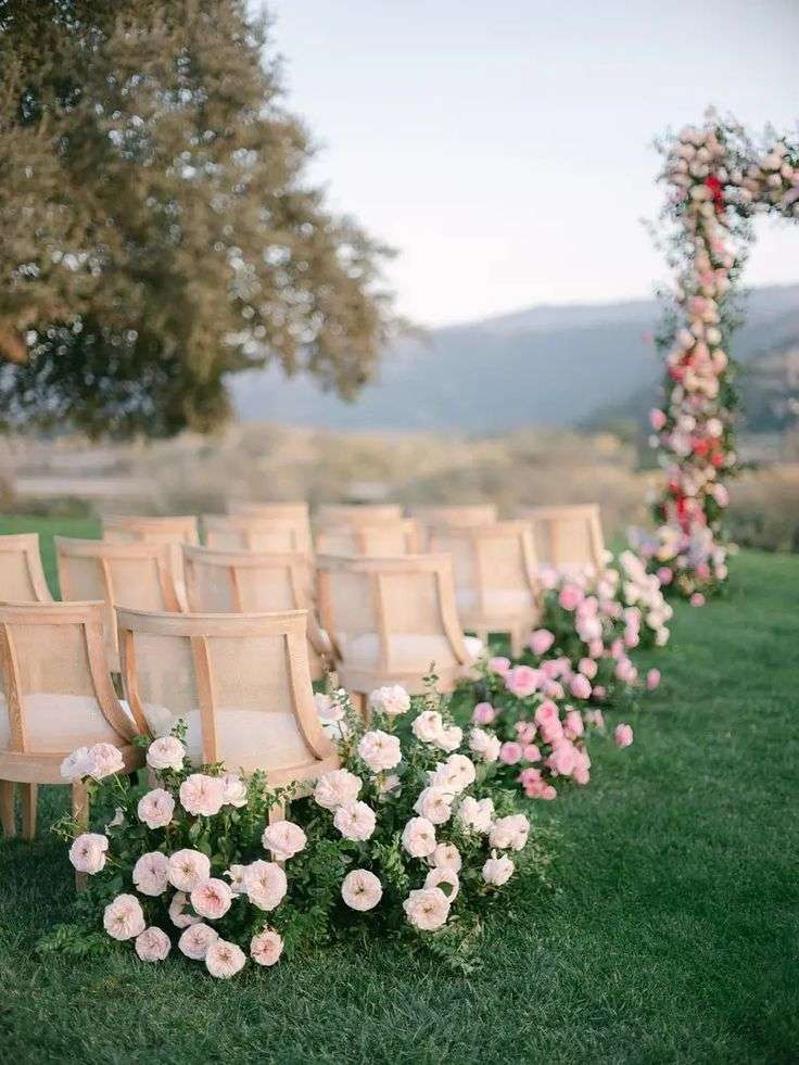 Blush garden rose aisle border leading to a colorful floral arch on a hillside