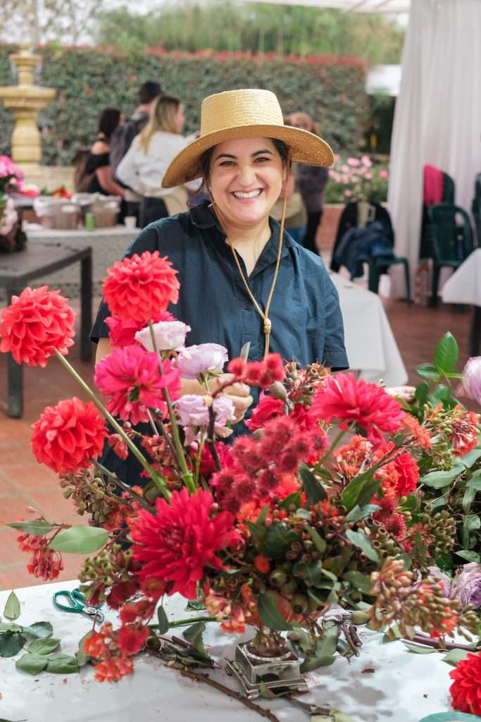Smiling designer in a straw hat arranging bright red dahlias and pink lisianthus