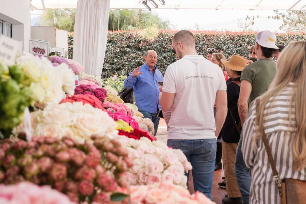 Farm host talking with visitors beside rows of freshly cut garden roses