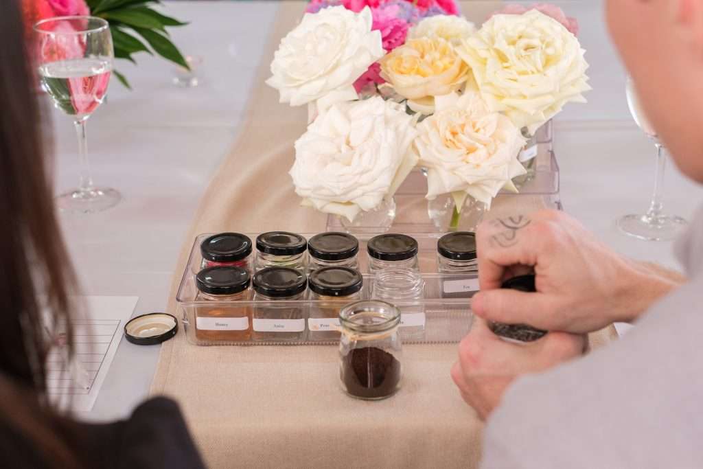 Guests smelling scent jars beside a vase of white and blush garden roses