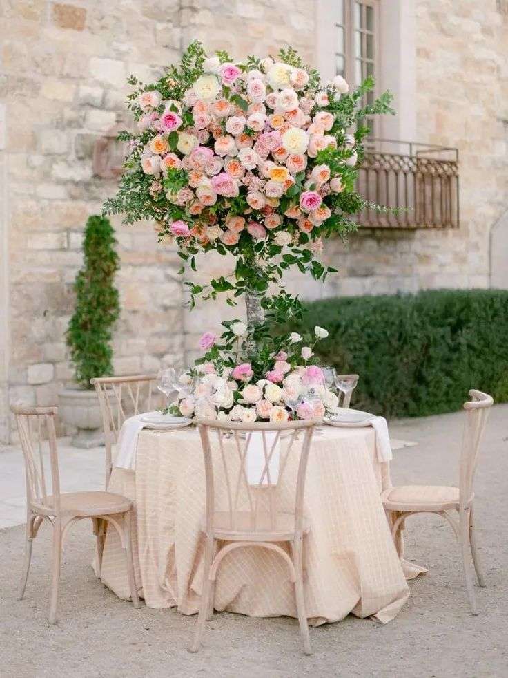 Tall pedestal centerpiece of blush and peach garden roses over a reception table
