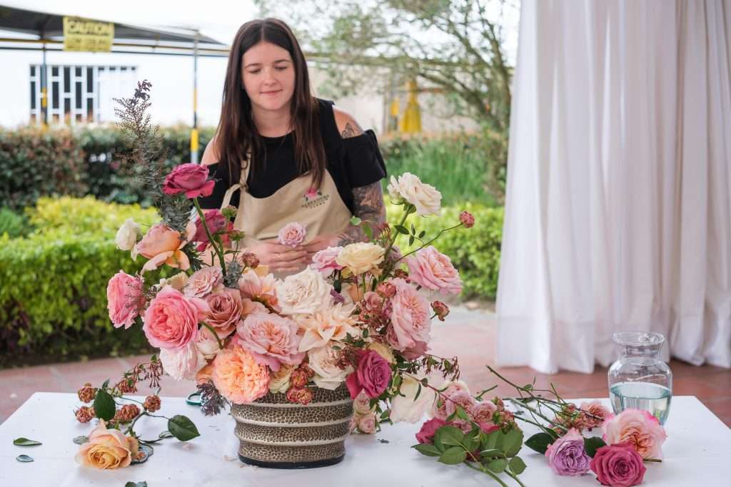 Designer building a lush pink and cream garden rose arrangement in a patterned vase