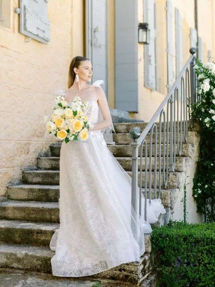 Bride in beaded gown descending stone steps with amber and cream garden rose bouquet